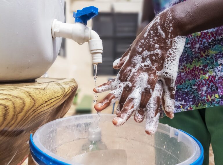 An African with foam on hands, washing hands under running water with from tap for protection against bacteria and viruses diseases